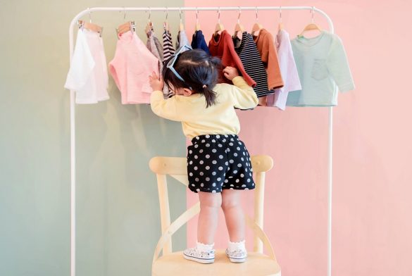 Soft Focus Of A Two Years Old Child Choosing Her Own Dresses From Kids Cloth Rack